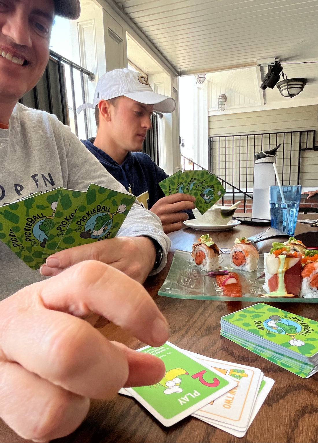 father and son playing the card game Pickleball Slam while eating sushi